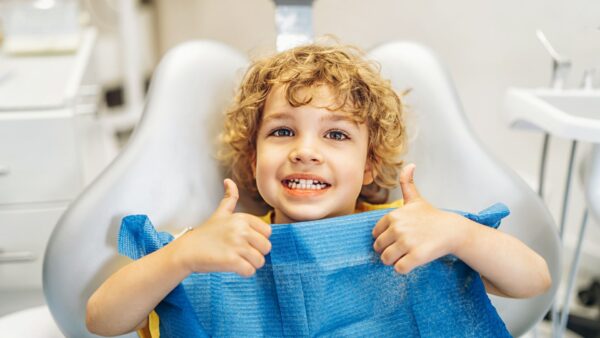 child sitting in dental chair smiling and giving thumbs up